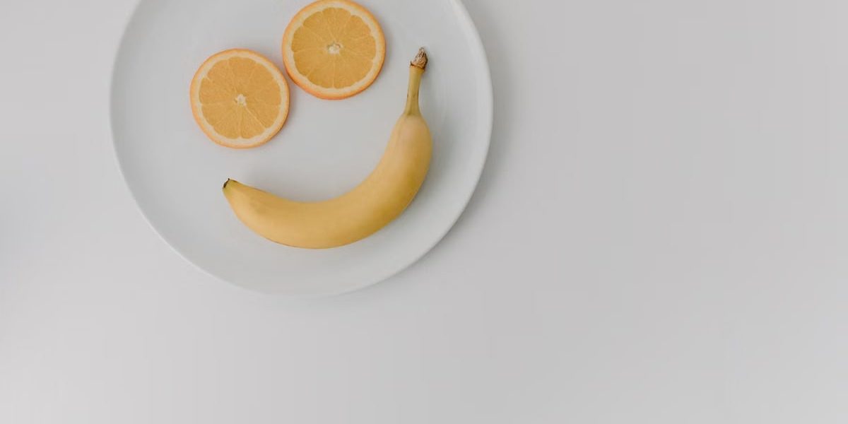 A playful arrangement of banana and orange slices forming a smile on a white plate.