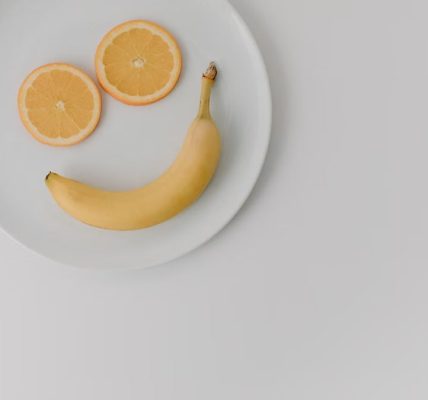 A playful arrangement of banana and orange slices forming a smile on a white plate.