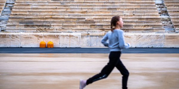 A girl runs in a historic stadium with empty stands, symbolizing youthful energy and ancient architecture.